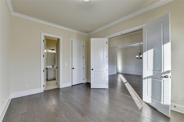 unfurnished bedroom with ensuite bath, dark wood-type flooring, ornamental molding, and a chandelier