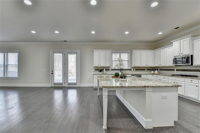 kitchen featuring ornamental molding, dark hardwood / wood-style flooring, light stone countertops, and an island with sink