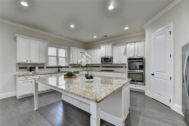 kitchen with light stone countertops, appliances with stainless steel finishes, white cabinets, and a kitchen island