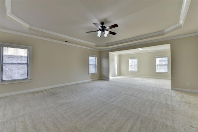 empty room featuring a raised ceiling, ornamental molding, plenty of natural light, and light colored carpet