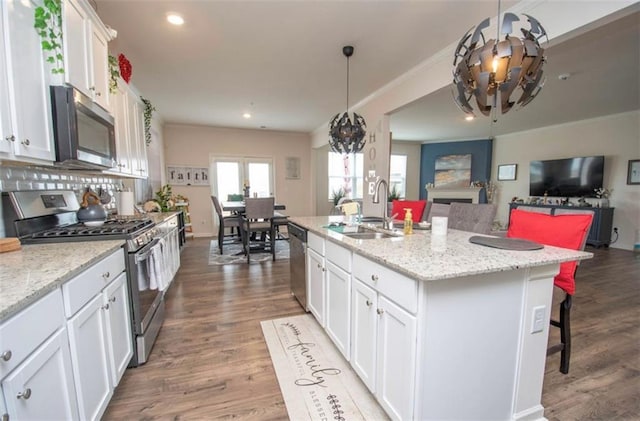 kitchen with a sink, a chandelier, stainless steel appliances, open floor plan, and white cabinetry
