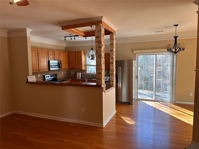 kitchen with dark wood-type flooring, appliances with stainless steel finishes, tasteful backsplash, decorative light fixtures, and kitchen peninsula