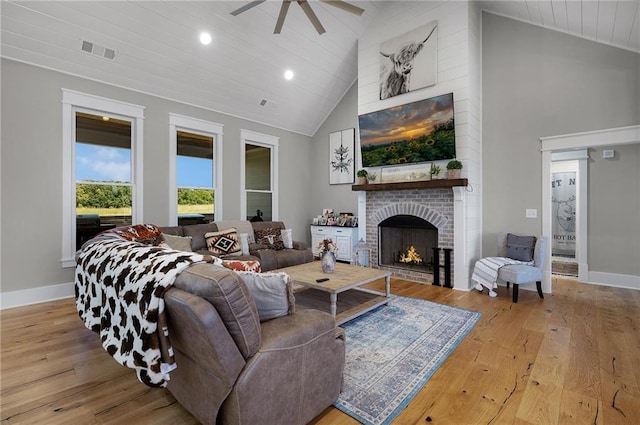 living room featuring ceiling fan, a fireplace, high vaulted ceiling, and light wood-type flooring