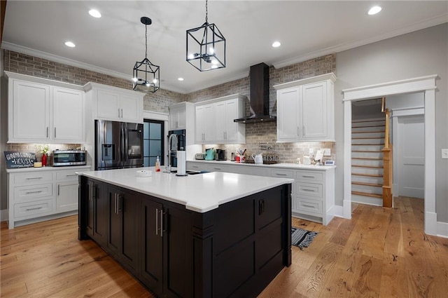 kitchen featuring wall chimney exhaust hood, white cabinetry, hanging light fixtures, appliances with stainless steel finishes, and a kitchen island with sink