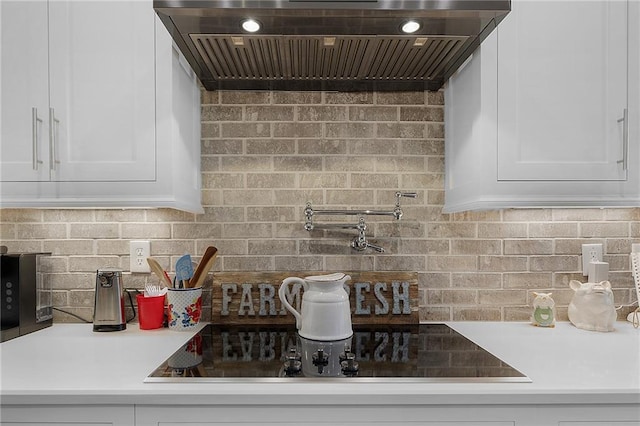 kitchen featuring black electric stovetop, range hood, and white cabinets