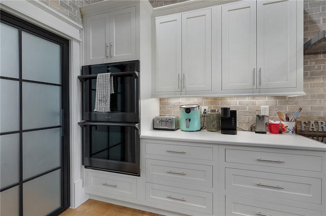 kitchen with backsplash, black double oven, light hardwood / wood-style floors, and white cabinets