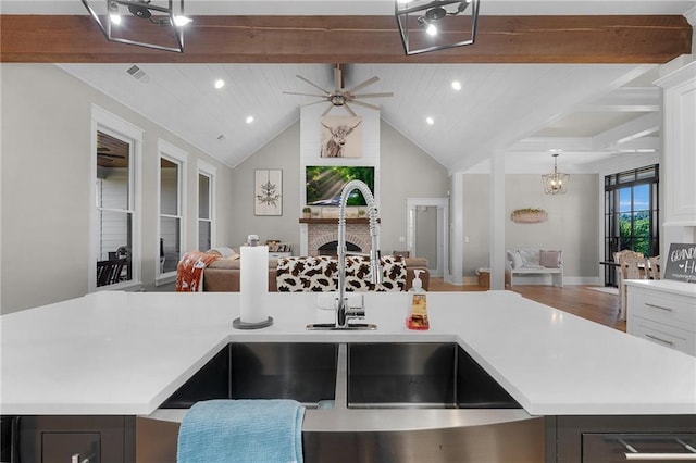 kitchen with sink, vaulted ceiling with beams, white cabinetry, a center island with sink, and ceiling fan