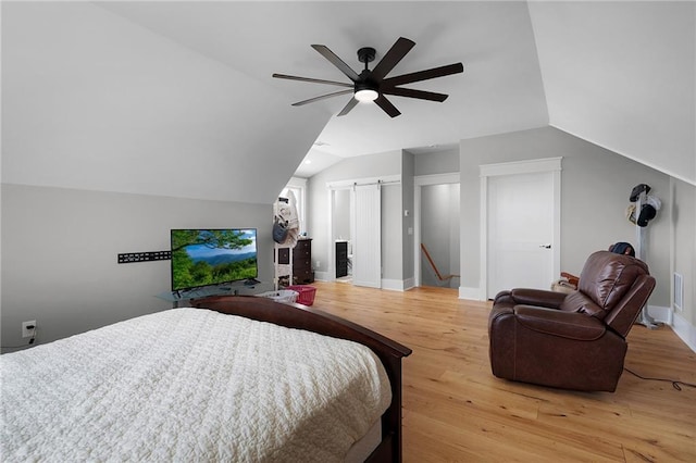 bedroom featuring ceiling fan, vaulted ceiling, a barn door, and wood-type flooring