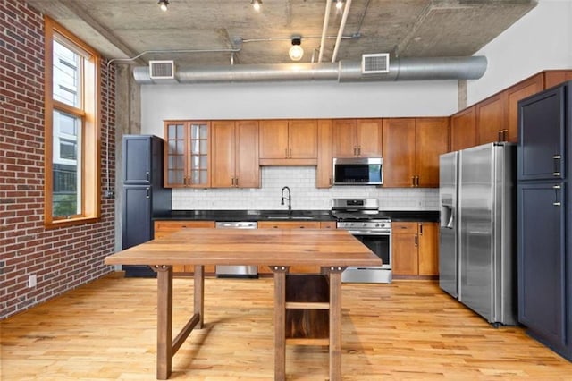 660 Glen Iris Drive # 206 & 109, Atlanta, GA 30308 - kitchen with appliances with stainless steel finishes, light wood finished floors, backsplash, brown cabinetry, and brick wall