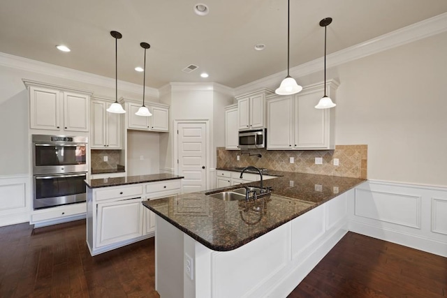 kitchen with kitchen peninsula, appliances with stainless steel finishes, sink, decorative light fixtures, and white cabinetry