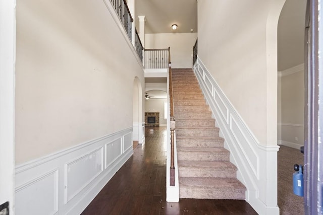 stairway with hardwood / wood-style flooring, ceiling fan, a stone fireplace, and a high ceiling