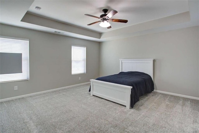 bedroom featuring a raised ceiling, light colored carpet, and baseboards