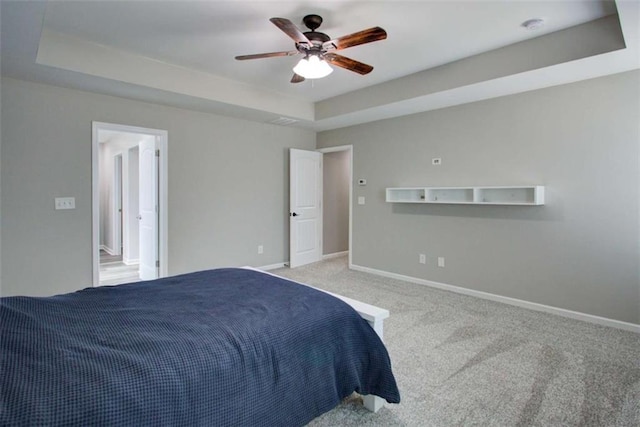 bedroom featuring light carpet, ceiling fan, a tray ceiling, and baseboards