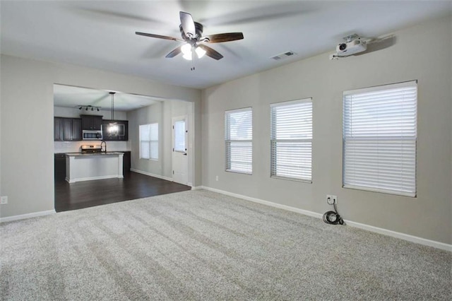 unfurnished living room with a sink, visible vents, a ceiling fan, baseboards, and dark colored carpet