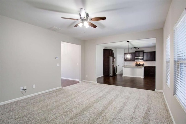 unfurnished living room featuring dark carpet, a ceiling fan, and baseboards