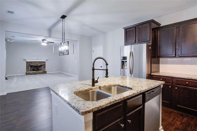 kitchen with stainless steel appliances, a fireplace, a sink, open floor plan, and a center island with sink