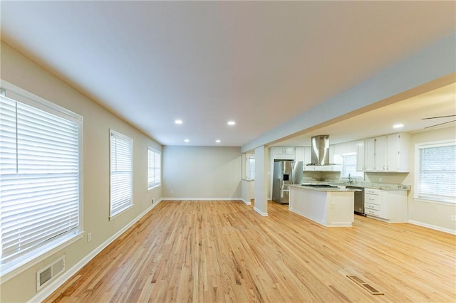 kitchen featuring light hardwood / wood-style flooring, wall chimney exhaust hood, stainless steel appliances, and a wealth of natural light