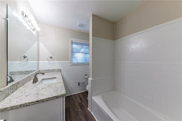 bathroom featuring wood-type flooring, tile walls, toilet, vanity, and a tub to relax in