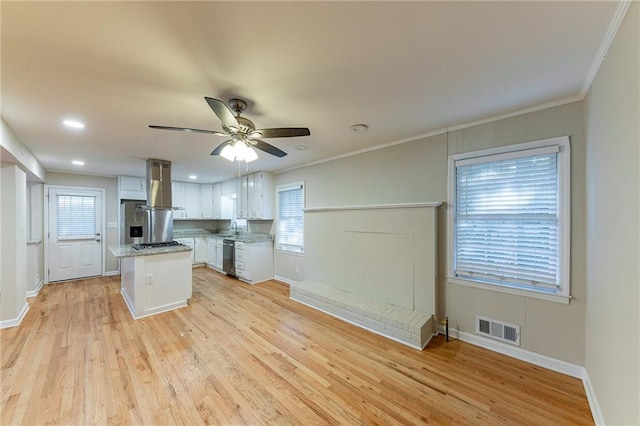 kitchen featuring a healthy amount of sunlight, wall chimney range hood, a center island, and white cabinets