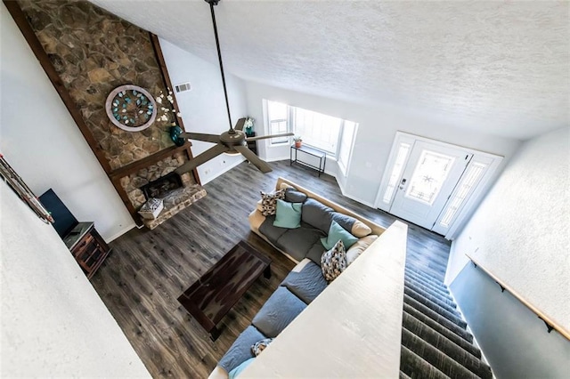 living room featuring vaulted ceiling, a stone fireplace, dark hardwood / wood-style floors, ceiling fan, and a textured ceiling