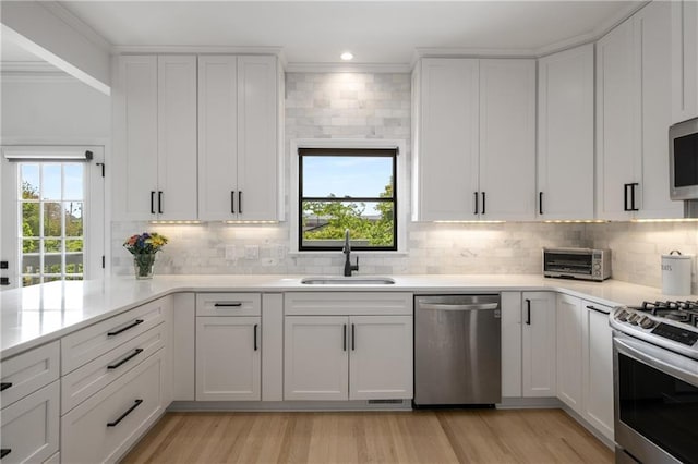 kitchen featuring a sink, decorative backsplash, crown molding, light countertops, and appliances with stainless steel finishes