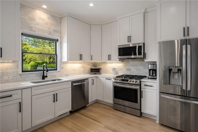 kitchen with a sink, light countertops, white cabinets, backsplash, and appliances with stainless steel finishes