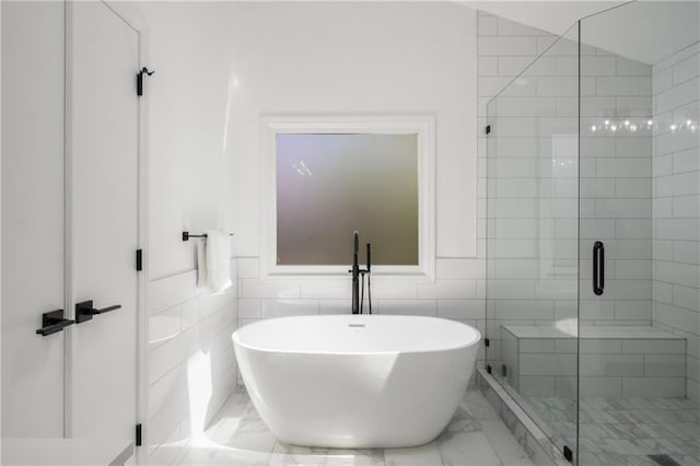 bathroom with marble finish floor, a freestanding bath, tile walls, and a stall shower
