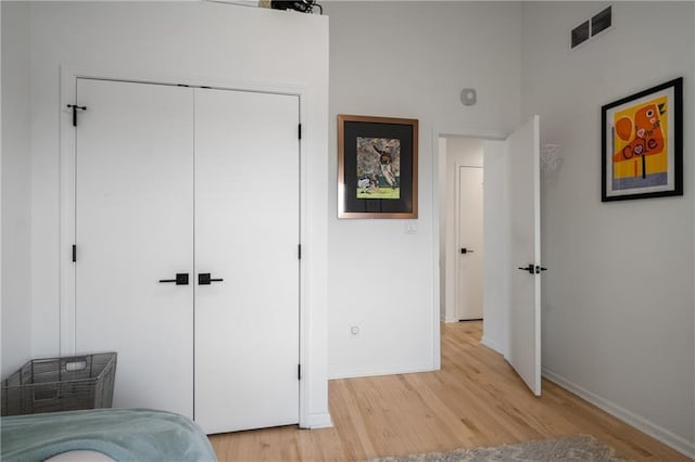 bedroom with baseboards, light wood-style flooring, visible vents, and a closet