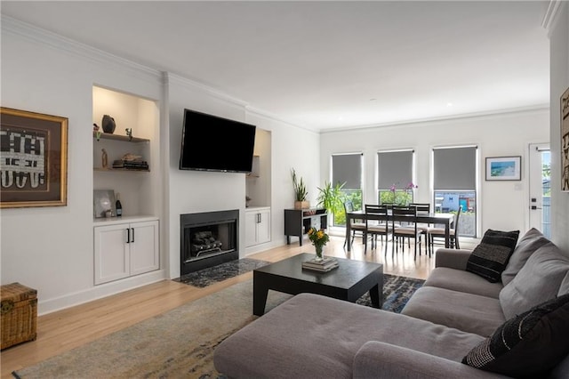 living room featuring a fireplace with flush hearth, wood finished floors, crown molding, and built in features
