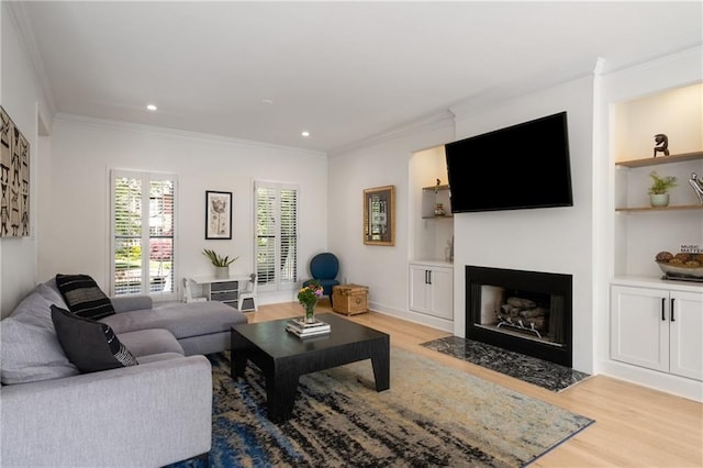 living area with light wood finished floors, a fireplace with flush hearth, recessed lighting, built in shelves, and crown molding