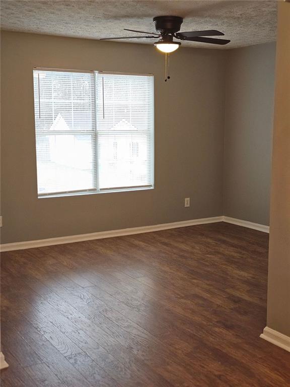 empty room with dark wood-type flooring, ceiling fan, and a textured ceiling