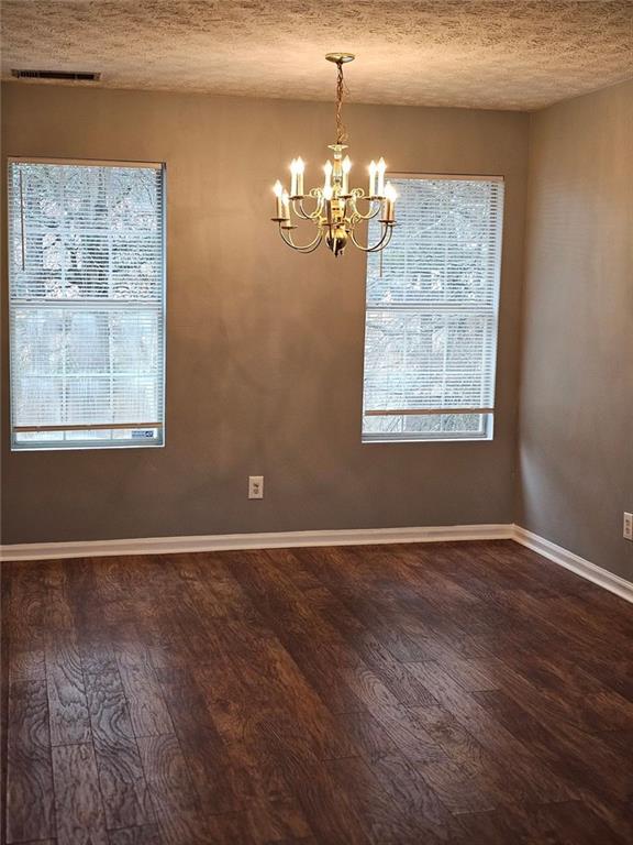 empty room featuring dark hardwood / wood-style floors, a notable chandelier, and a textured ceiling