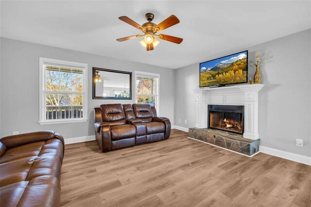 living room featuring a stone fireplace, light hardwood / wood-style flooring, and ceiling fan