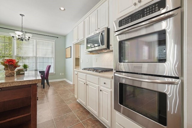 kitchen with appliances with stainless steel finishes, backsplash, light tile patterned floors, a chandelier, and white cabinetry