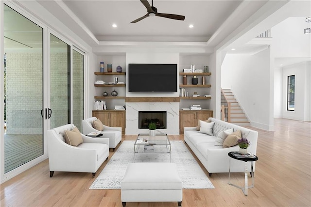 living room with ceiling fan, a raised ceiling, light hardwood / wood-style flooring, and a fireplace