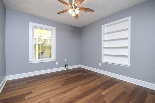 spare room with ceiling fan, dark hardwood / wood-style floors, built in features, and a textured ceiling