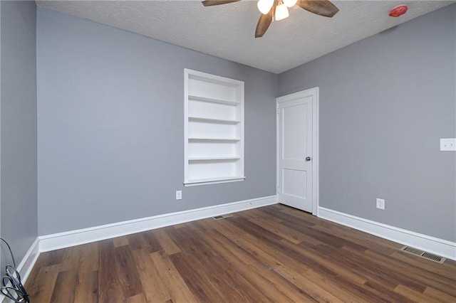 unfurnished room featuring ceiling fan, built in shelves, dark hardwood / wood-style floors, and a textured ceiling