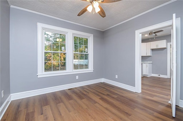 empty room with a textured ceiling, dark wood-type flooring, ornamental molding, and ceiling fan