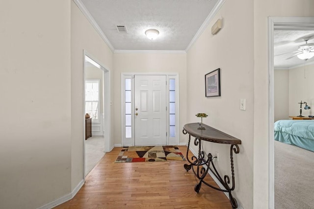 entrance foyer with visible vents, ornamental molding, light wood-style floors, a textured ceiling, and baseboards