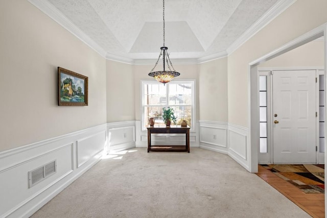 carpeted dining space with a tray ceiling, visible vents, a decorative wall, and a textured ceiling