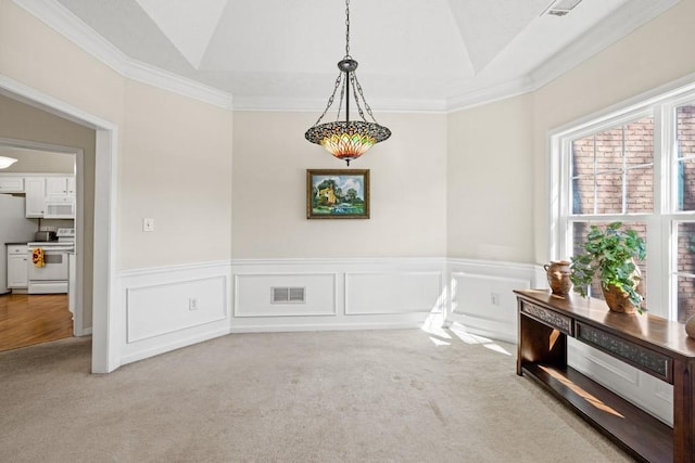 dining room with light carpet, visible vents, a raised ceiling, wainscoting, and a decorative wall