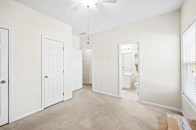 unfurnished bedroom featuring light colored carpet, visible vents, a textured ceiling, ensuite bath, and baseboards