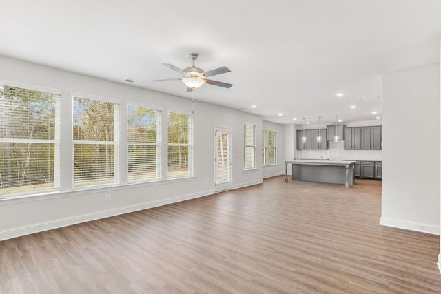 unfurnished living room with ceiling fan, light wood-type flooring, and sink