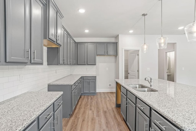 kitchen featuring sink, decorative backsplash, gray cabinets, light wood-type flooring, and decorative light fixtures