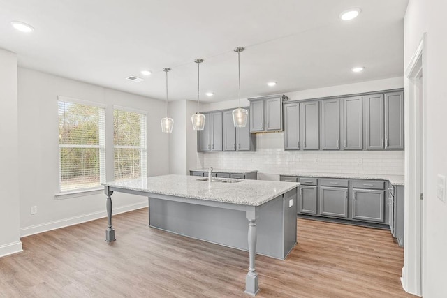 kitchen with a center island with sink, gray cabinetry, light wood-type flooring, and sink