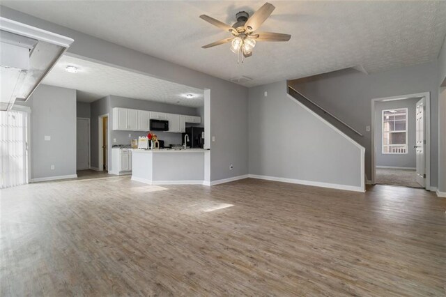 living room featuring hardwood / wood-style flooring, ceiling fan, a large fireplace, and a textured ceiling