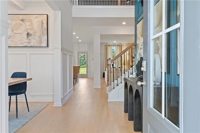 foyer entrance with stairs, a decorative wall, light wood-type flooring, and wainscoting