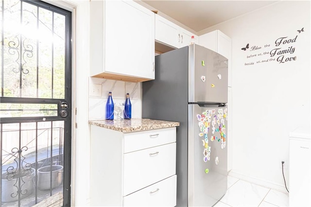 kitchen featuring baseboards, freestanding refrigerator, light stone counters, and white cabinets