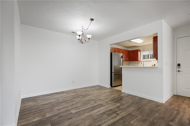 kitchen with a chandelier, hardwood / wood-style floors, stainless steel refrigerator, and kitchen peninsula