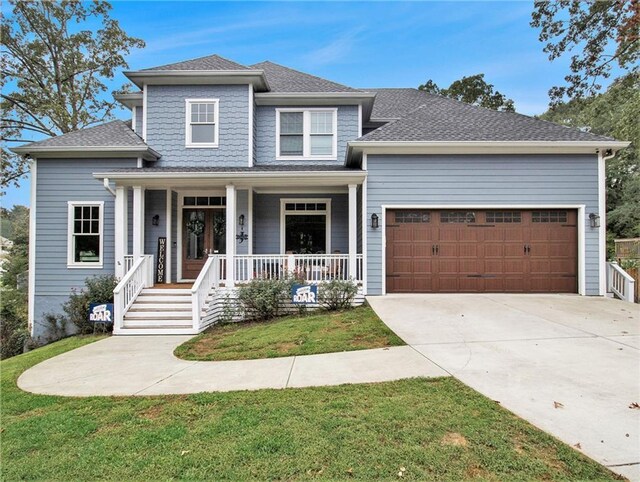 view of front facade with a garage, driveway, roof with shingles, covered porch, and a front yard